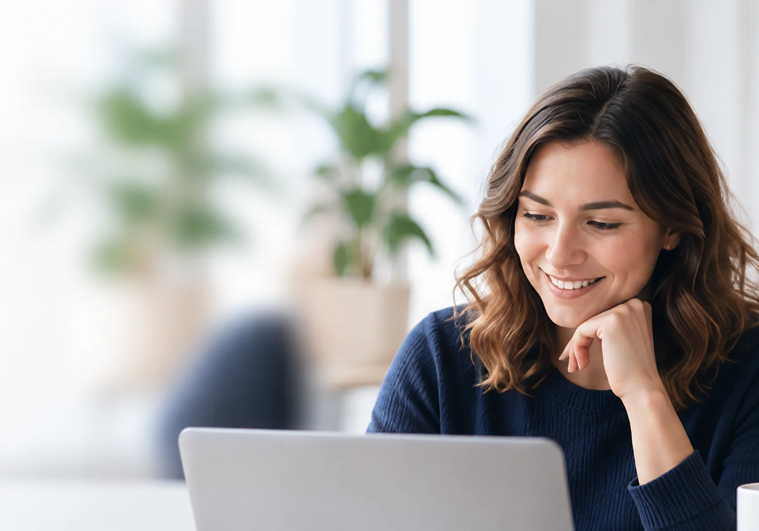 A business professional reviewing work on a laptop in a bright, modern office.